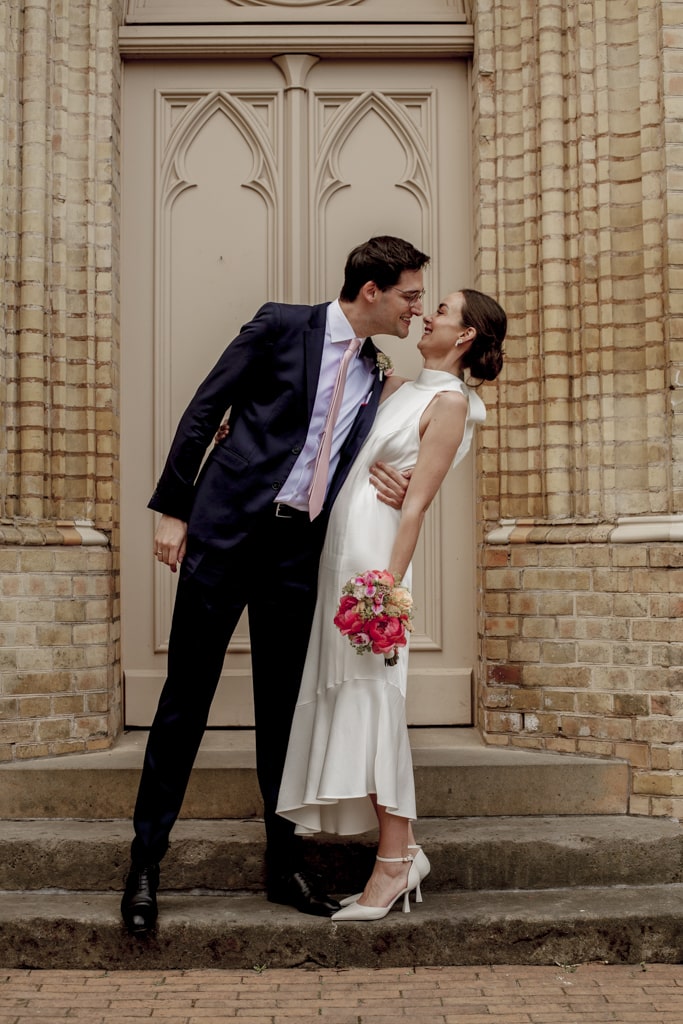 Hochzeitsfotograf Oldenburg Brautpaar küsst sich lächelnd vor der Kirche