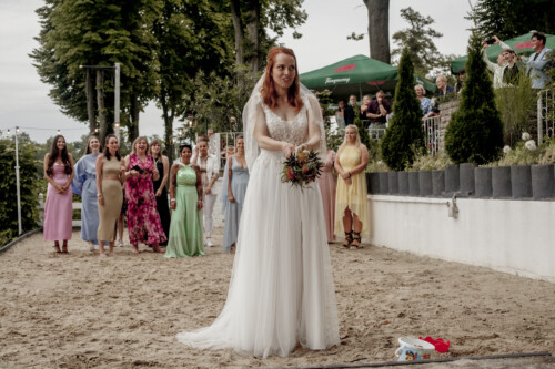Hochzeitsfotograf Berlin Braut wirkt den Brautstrauss und die Gäste jubeln im Hintergrund in Richtershorn am See